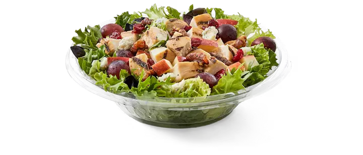 A delightful Potbelly Menu item, the Apple Walnut Salad, featuring a vibrant bowl of field greens topped with all-natural grilled chicken breast, crumbled blue cheese, juicy grapes, crisp apples, dried cranberries, and candied walnuts, drizzled with tangy balsamic vinaigrette, served in a clear bowl against a black background, priced at $10.99 with 687 calories.