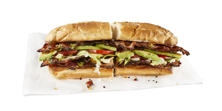 A classic Potbelly Menu item, the BLTA, featuring a toasted sub roll filled with crispy applewood smoked bacon, fresh lettuce, juicy tomatoes, and creamy fresh-sliced avocado, cut into portions and served on white paper against a black background, priced at $11.79 with 612 calories.