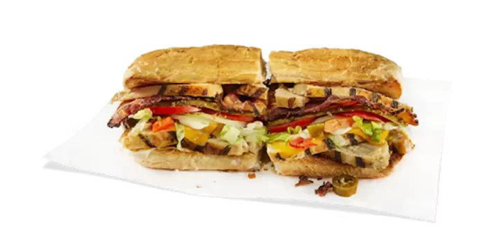 A savory Potbelly Menu item, the Chicken Club, featuring a toasted sub roll filled with all-natural grilled chicken, applewood smoked bacon, melted cheddar cheese, and fresh lettuce, tomatoes, and peppers, cut into portions and served on white paper against a black background, priced at $12.29 with 690 calories.