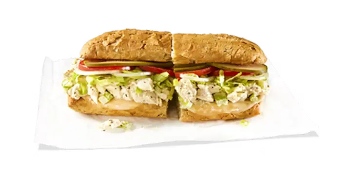 A creamy Potbelly Menu item, the Chicken Salad, featuring a toasted sub roll filled with homemade chicken salad, melted provolone cheese, crisp lettuce, tomatoes, and pickles, cut into portions and served on white paper against a black background, priced at $10.89 with 761 calories.