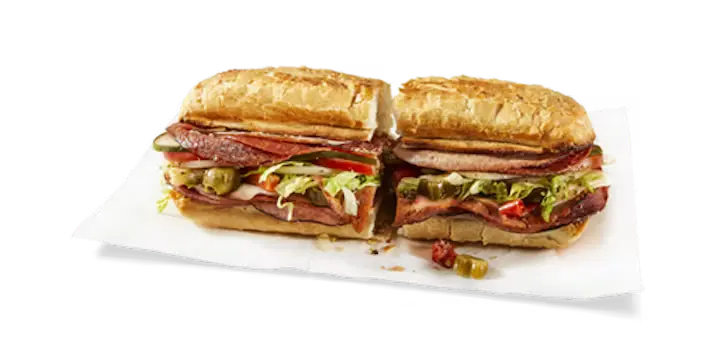 A robust Potbelly Menu item, the Italian, featuring a toasted sub roll packed with salami, old-world capicola, pepperoni, mortadella, and melted provolone cheese, layered with fresh lettuce, tomatoes, and pickles, cut into portions and served on white paper against a black background, priced at $11.29 with 774 calories.