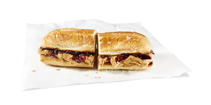 A nostalgic Potbelly Menu item, the PB&J, featuring a toasted sub roll filled with creamy peanut butter and sweet grape jelly, cut into portions and served on white paper against a black background, priced at $9.99 with 605 calories.