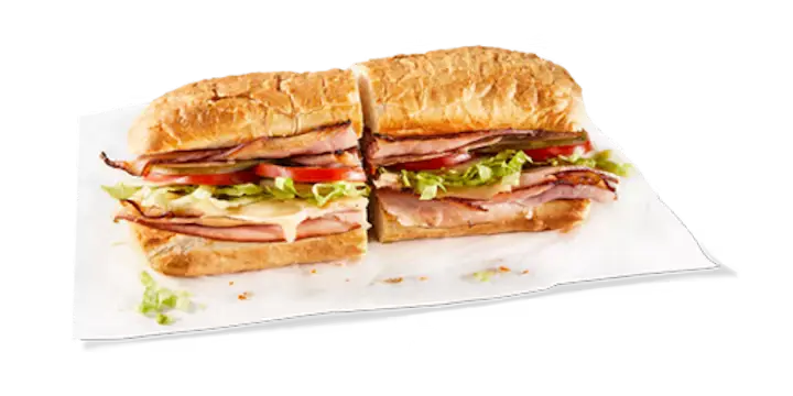 A classic Potbelly Menu item, the Smoked Ham, featuring a toasted sub roll filled with hickory smoked ham, melted Swiss cheese, fresh lettuce, tomatoes, and onions, cut into portions and served on white paper against a black background, priced at $10.89 with 712 calories.