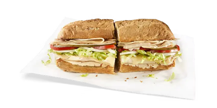 A simple yet tasty Potbelly Menu item, the Turkey Breast, featuring a toasted sub roll filled with hand-sliced turkey breast, melted Swiss cheese, fresh lettuce, tomatoes, and onions, cut into portions and served on white paper against a black background, priced at $10.89 with 638 calories.