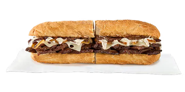 A hearty Potbelly Menu item, the Prime Rib Steak, featuring a toasted sub roll filled with tender sliced prime rib steak, melted Swiss cheese, housemade caramelized onions, and garlic aioli, cut into portions and served on white paper against a black background, priced at $13.29 with 715 calories.